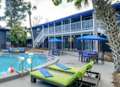 Thumbnail 1 of 23 - Community pool at Mandarin Bay Apartments in Jacksonville, FL surrounded by lime green lounge chairs and patio tables with blue umbrellas.