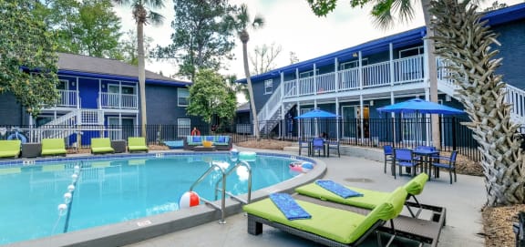 Community pool at Mandarin Bay Apartments in Jacksonville, FL surrounded by lime green lounge chairs and patio tables with blue umbrellas.