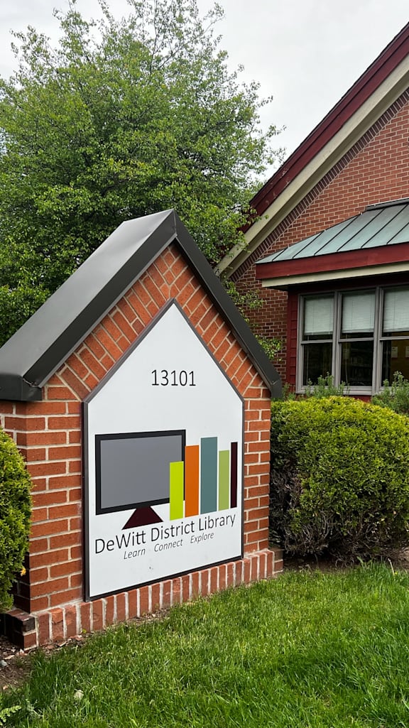 A sign for DeWitt District Library is in front of a brick building.