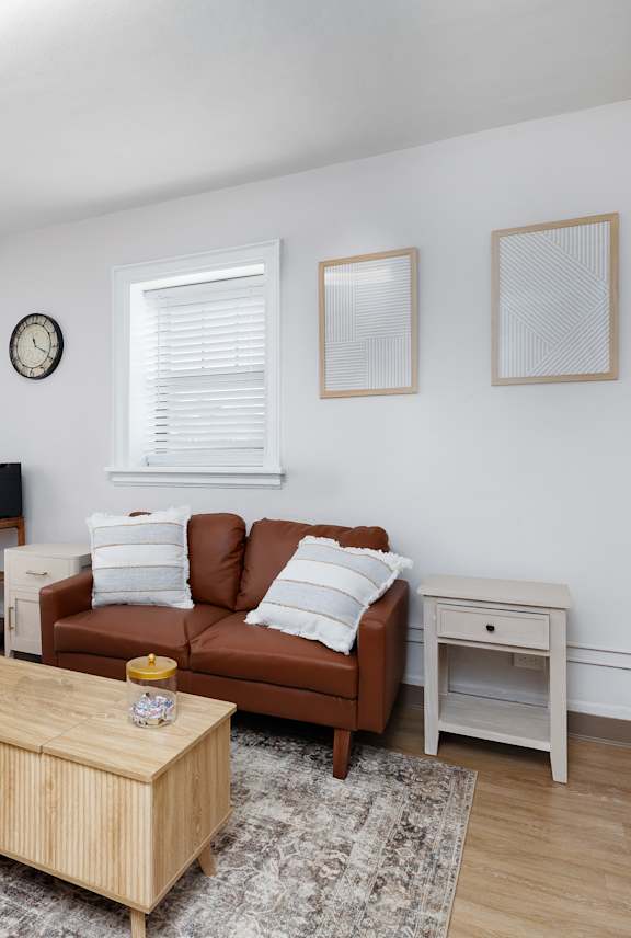 A living room with a brown couch, a wooden coffee table, and a small white table.