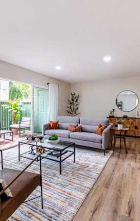 A living room with a grey sofa, a glass coffee table, and a wooden floor.