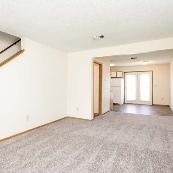 A spacious room with a staircase on the left and a doorway leading to another room on the right.