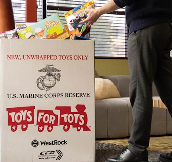 A man is handing over a box of unwrapped toys to the U.S. Marine Corps Reserve Toys for Tots program.