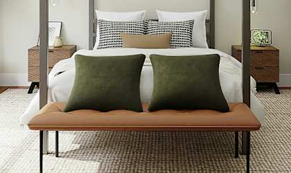 A bedroom with a bed, two pillows, a bench, and two plants.