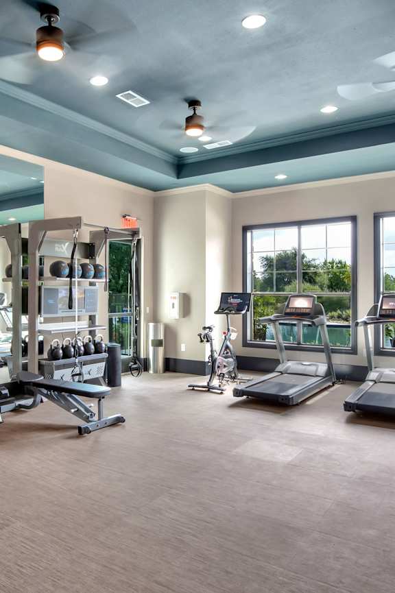 a large fitness room with cardio equipment and windows