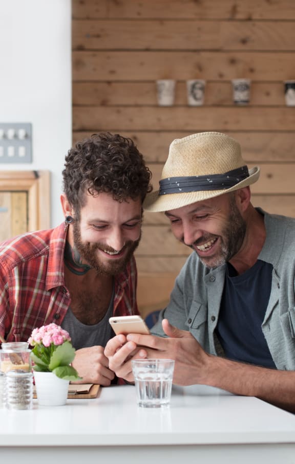 two men sitting at a table looking at a cell phone