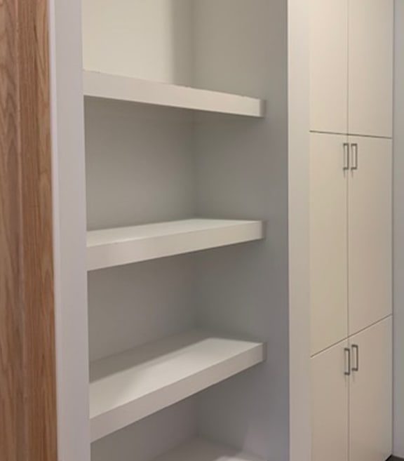 A white bathroom with a toilet and a shelving unit.