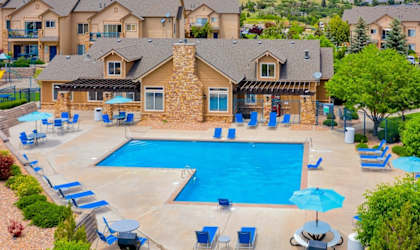 A large swimming pool surrounded by blue lounge chairs and umbrellas in a residential area.