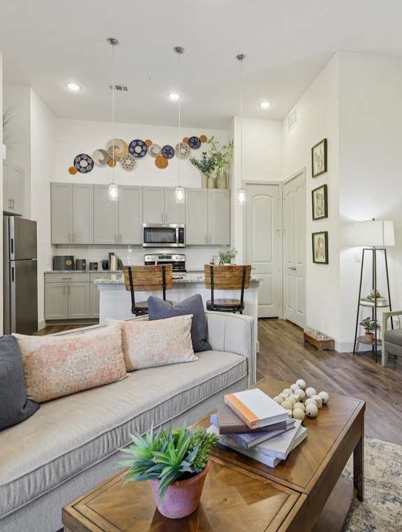 A modern living room with a grey couch, a wooden coffee table, and a kitchen area in the background.