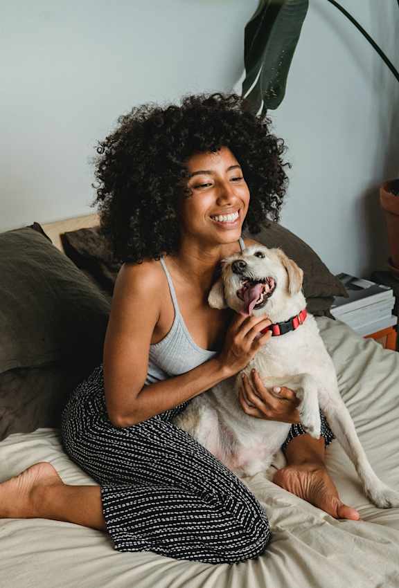 A woman with curly hair is sitting on a bed with a dog.