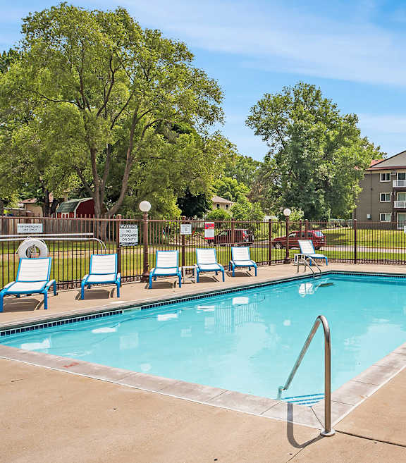 A pool surrounded by sun loungers and trees.