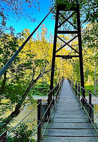 A wooden bridge with metal railings spans over a body of water surrounded by trees.at Forge Overlook, Halethorpe Maryland