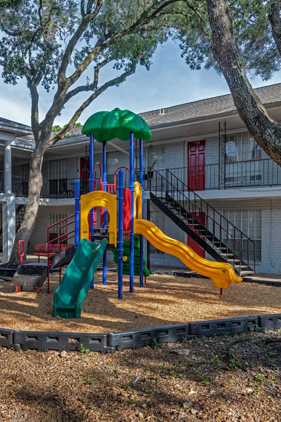 A playground with a green slide and a yellow slide in front of a building.