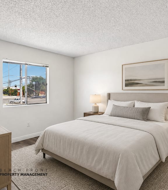 A well-lit bedroom with a large bed, a nightstand with a lamp, and a framed picture on the wall.