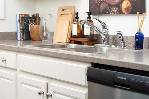 A kitchen with a black dishwasher and a wooden soap holder at The Bosk Apartment Homes, Woodbury