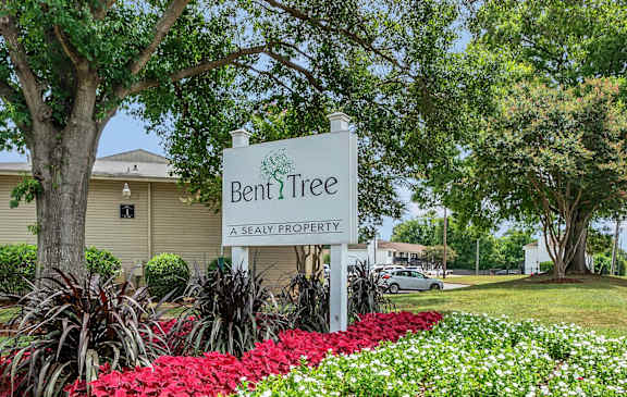 A sign that says Bent Tree stands in front of a flower bed.