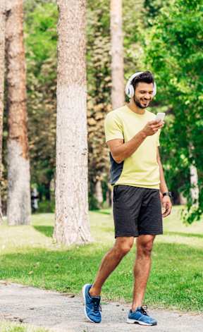 A man in a yellow shirt and blue shoes is walking on a path in a park.