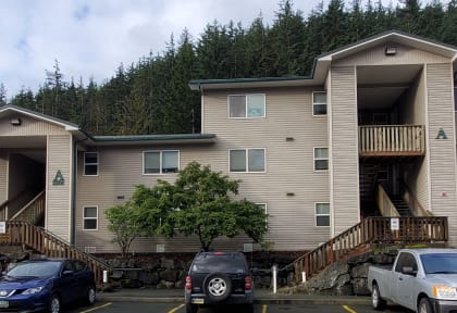 A row of apartment buildings with cars parked in front.