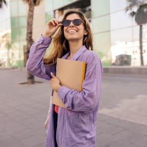 a young woman wearing sunglasses and holding a notebook and smiling
