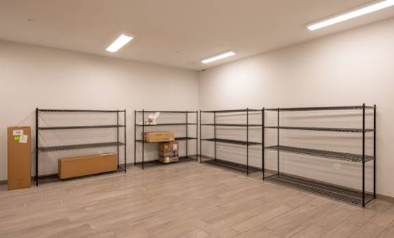 A room with a white wall and a wooden floor with a shelf and a box on it.