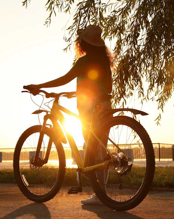 a woman standing next to her bike with the sun shining through a tree
