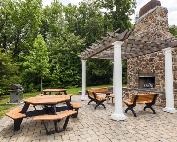 a patio with a stone fireplace and a pergola with benches and tables at Chesapeake Ridge, Maryland
