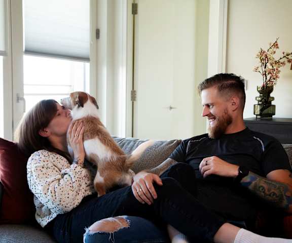 A man and woman sitting on a couch with a dog between them.