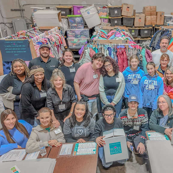 A group of people are gathered around a table with boxes in a warehouse setting. at Lakes Edge Apartments, North Carolina