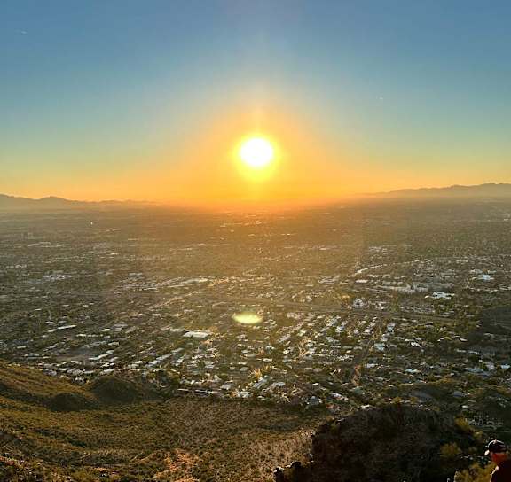 A person is standing on a hill overlooking a cityscape at sunset.