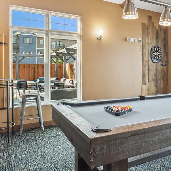 A pool table in a room with a bar stool and a clock on the wall.