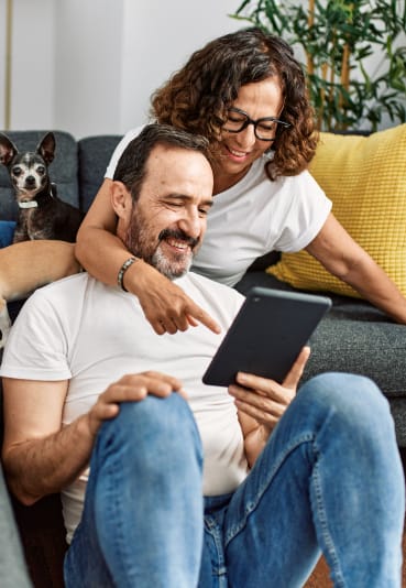 a couple sitting on a couch with their dogs and looking at a tablet at Casa Blanca Apartment Homes, Washington