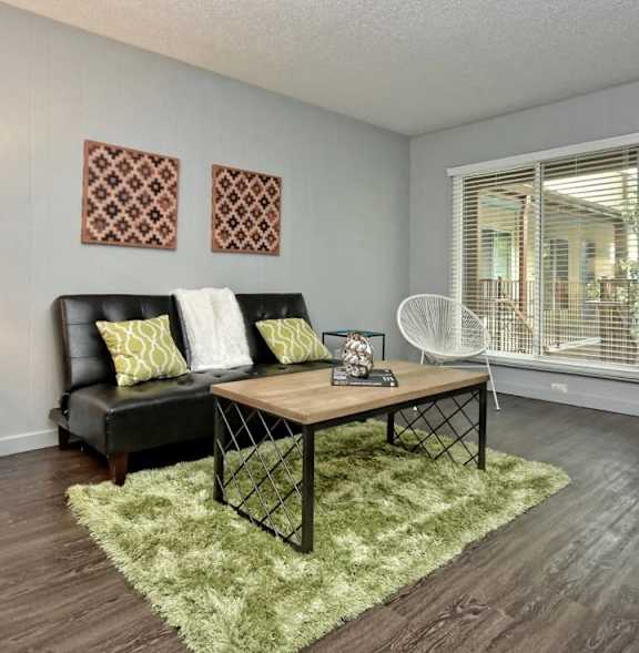 A living room with a black couch and a green rug.