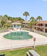 A pool surrounded by a fence and benches in front of apartment buildings.