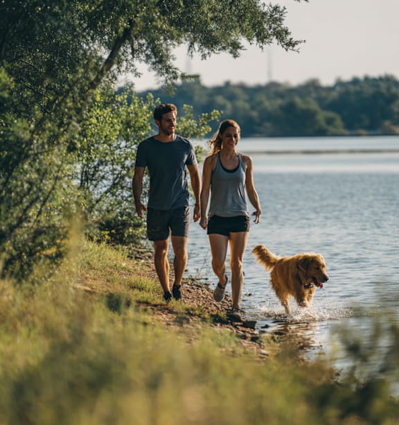 A man and woman walking a dog along a lake.