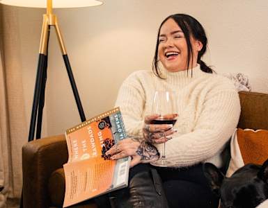 three women sitting on a couch drinking wine and reading books
