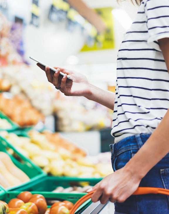 A person holding a phone and a shopping cart in a grocery store.