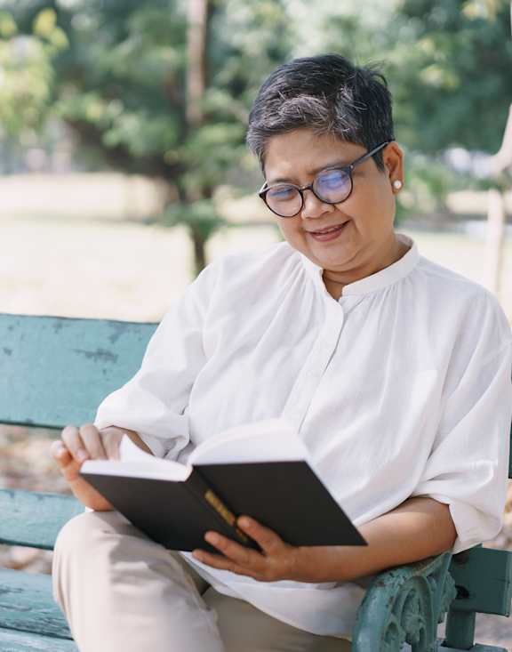 A person is sitting on a bench reading a book.