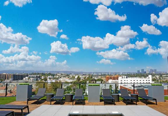 a rooftop terrace with lounge chairs and a view of the city