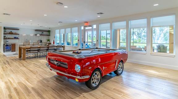 A red car is parked in a spacious room with wooden floors and large windows.