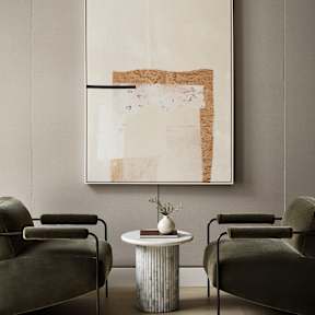 Two chairs and a table are in front of a framed artwork.