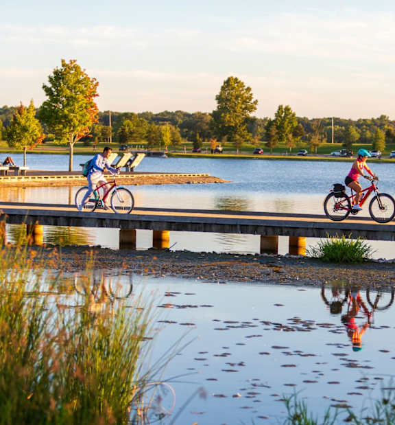 Two people riding bikes on a bridge over a lake.