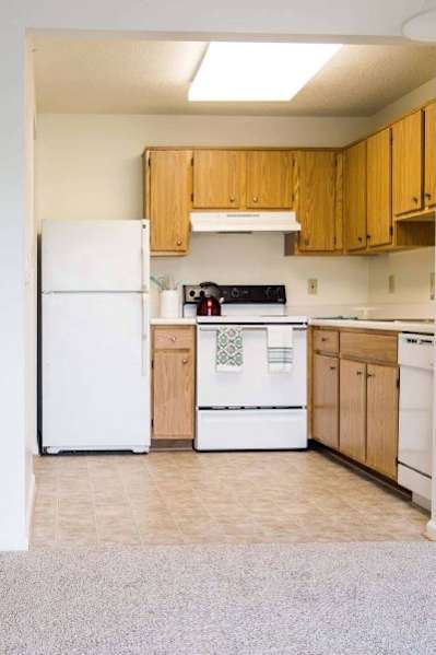 an empty kitchen with white appliances and wooden cabinets at Greenbrier Seniors Apartments, Virginia