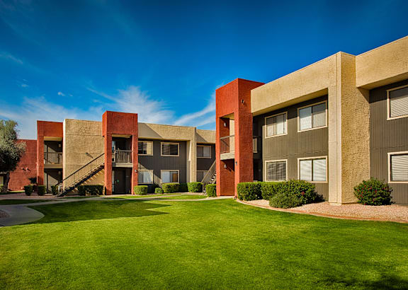 A modern building with a red and beige facade and a green lawn in front.