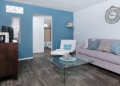 Thumbnail 1 of 23 - Modern living room in fifteen 50 apartments Las Vegas with grey plank tile floor, grey sofa, glass coffee table, and blue accent wall.