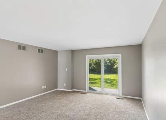 A room with a carpeted floor and a sliding glass door leading to a green outdoor area.