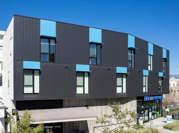 A modern building with a black and blue exterior is surrounded by parked cars.