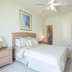 Two-bedroom bedroom at Hawthorne Apartment Homes with white bedding, ceiling fan, and wall artwork.