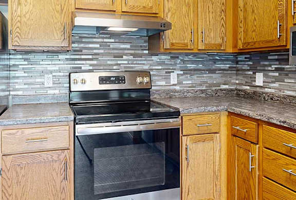 a kitchen with stainless steel appliances, wood cabinetry, and tile backsplash