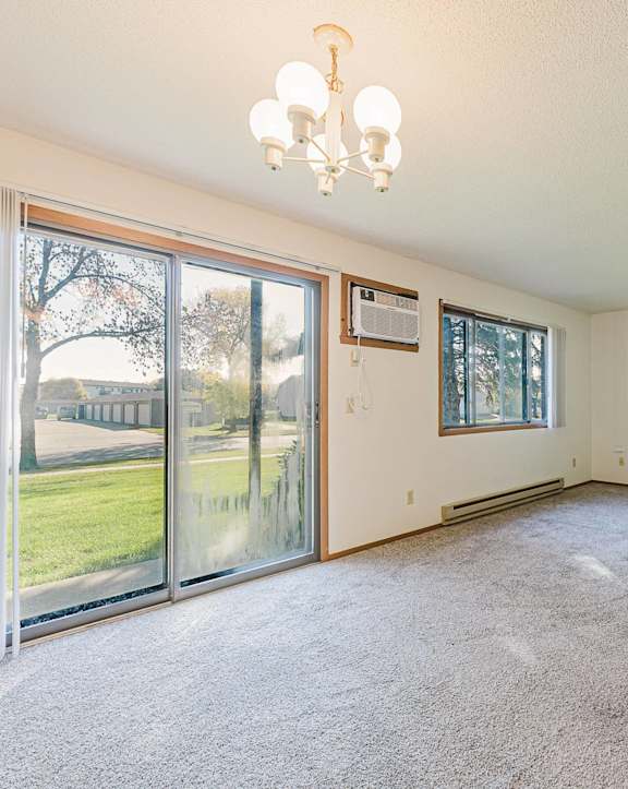 A large, empty room with a chandelier and a window overlooking a green lawn.