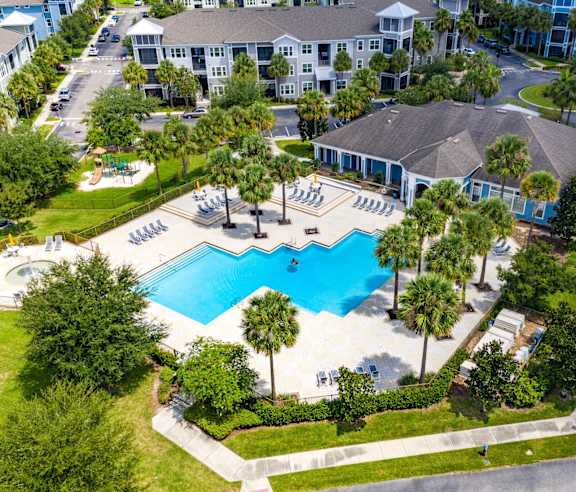 An aerial view of a pool surrounded by palm trees and a resort.